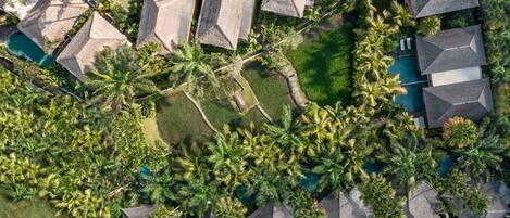An aerial view of a resort with multiple bungalow-style buildings, a central swimming pool, and lush tropical landscaping.