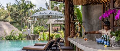 A poolside bar with lounge chairs, a bar counter, and a tropical setting with palm trees and a pool.