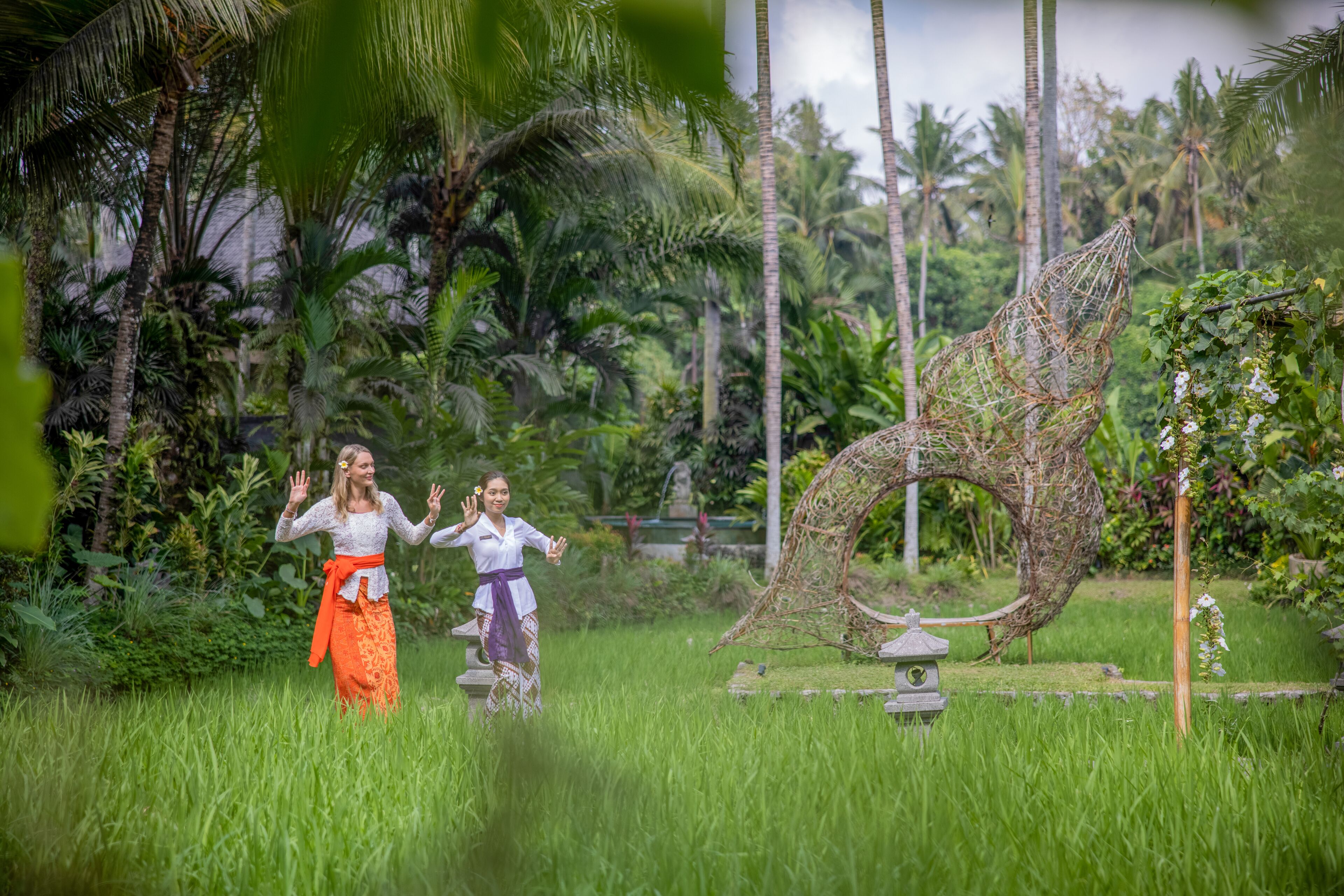 A tropical garden with a stone sculpture and two people in traditional attire.