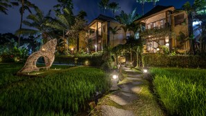 A well-lit, modern hotel with a pathway leading to the entrance, surrounded by lush greenery and palm trees. - The Sankara Resort & Spa (Ubud)
