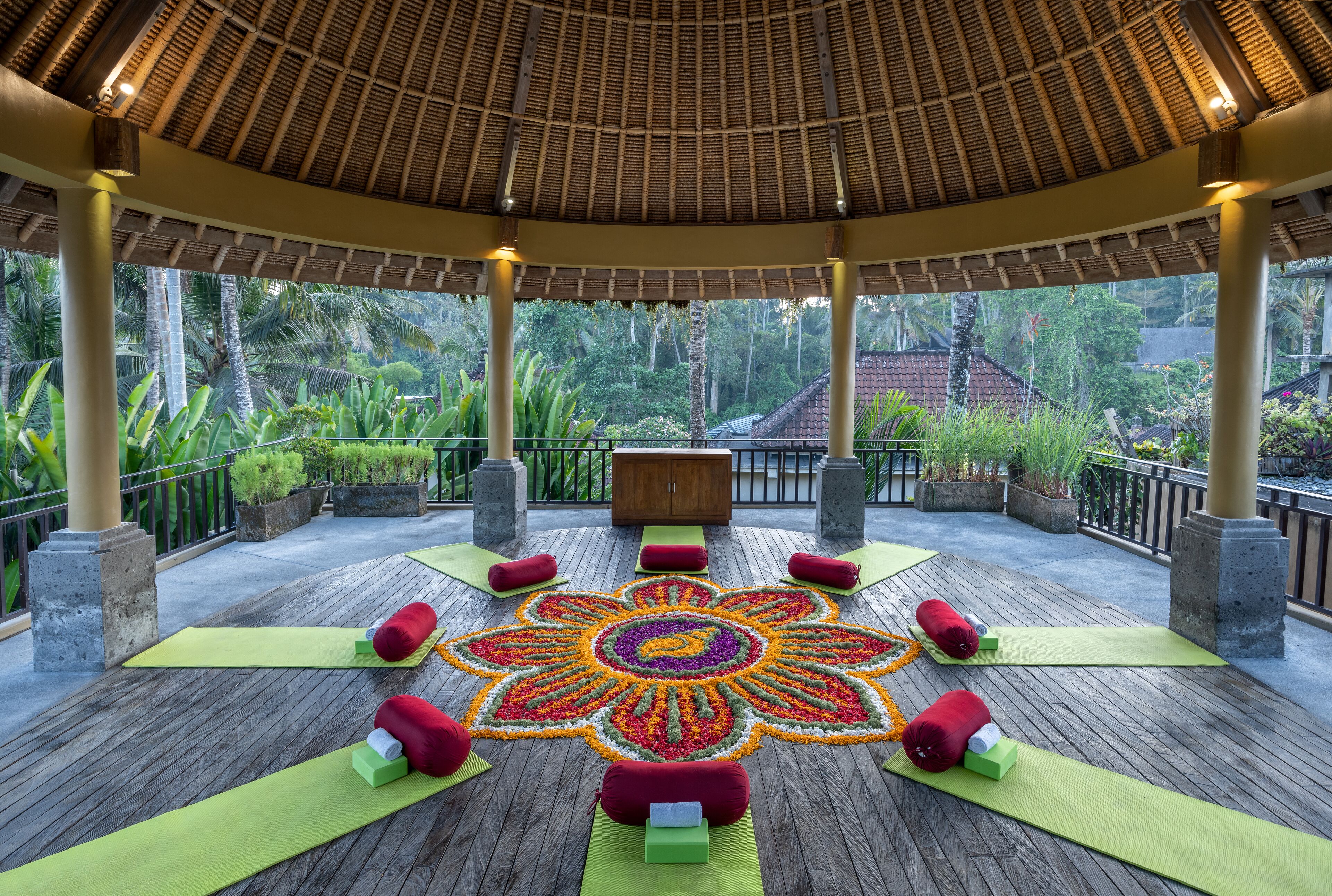A covered outdoor area with a wooden deck, green mats, and red cushions arranged in a circular pattern.