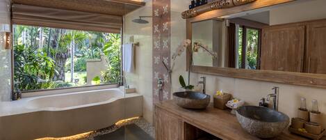 A modern bathroom with a large bathtub, two stone sinks, a wooden vanity, and a large mirror.