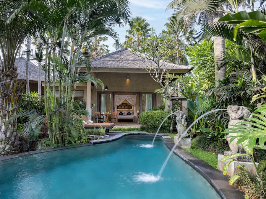 Una piscina con cascada, rodeada de exuberante vegetación tropical y un edificio con zona de estar cubierta.