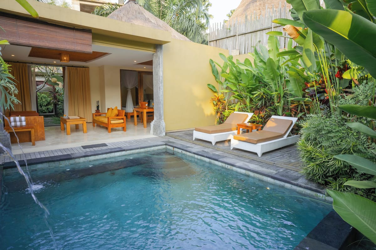 A pool area with lounge chairs, a wooden deck, and tropical plants.