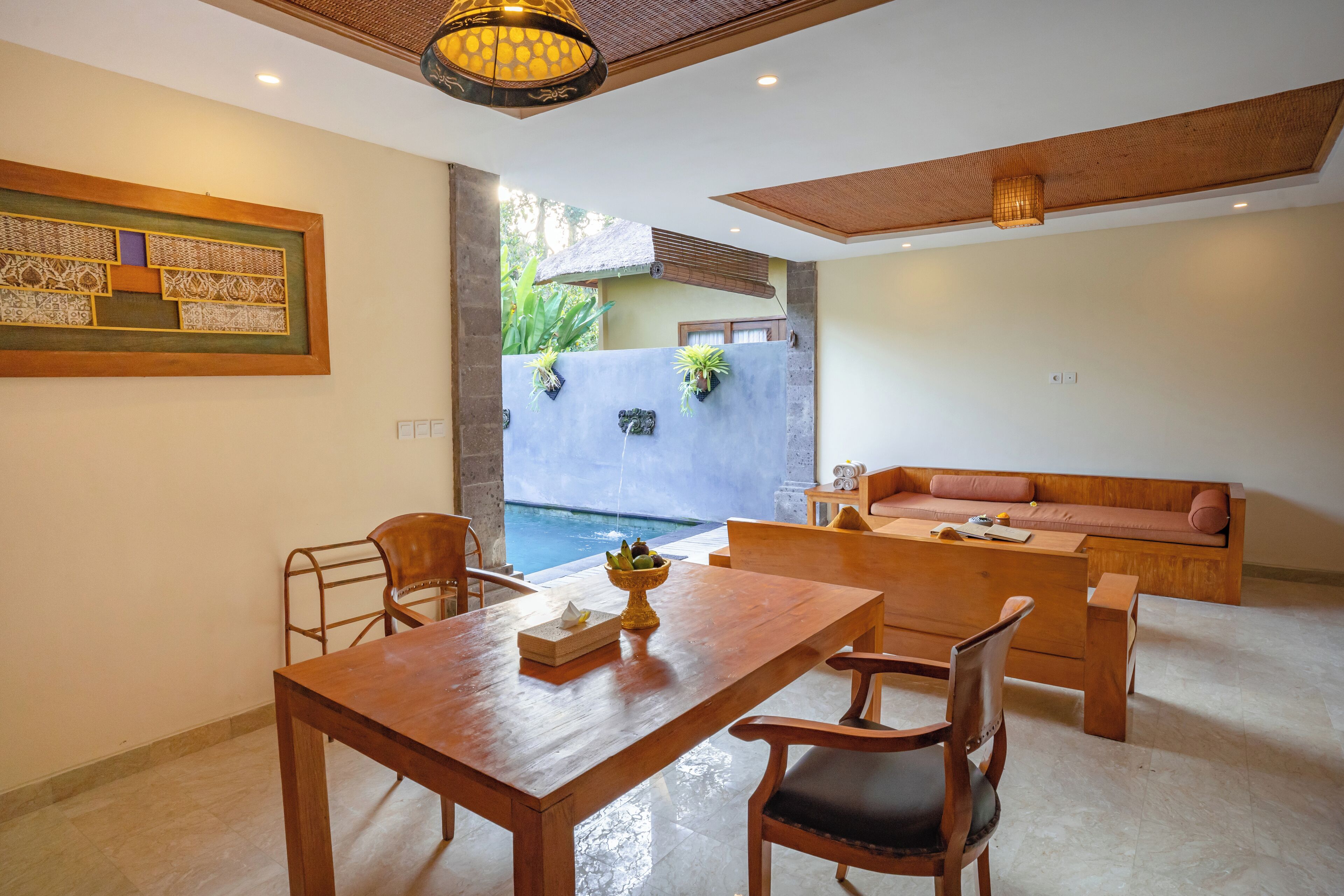A dining area with a wooden table and chairs, a sofa, and a view of a swimming pool.