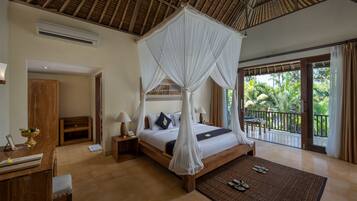 A spacious bedroom with a large bed, a wooden desk, a chair, and a balcony with a view of palm trees.