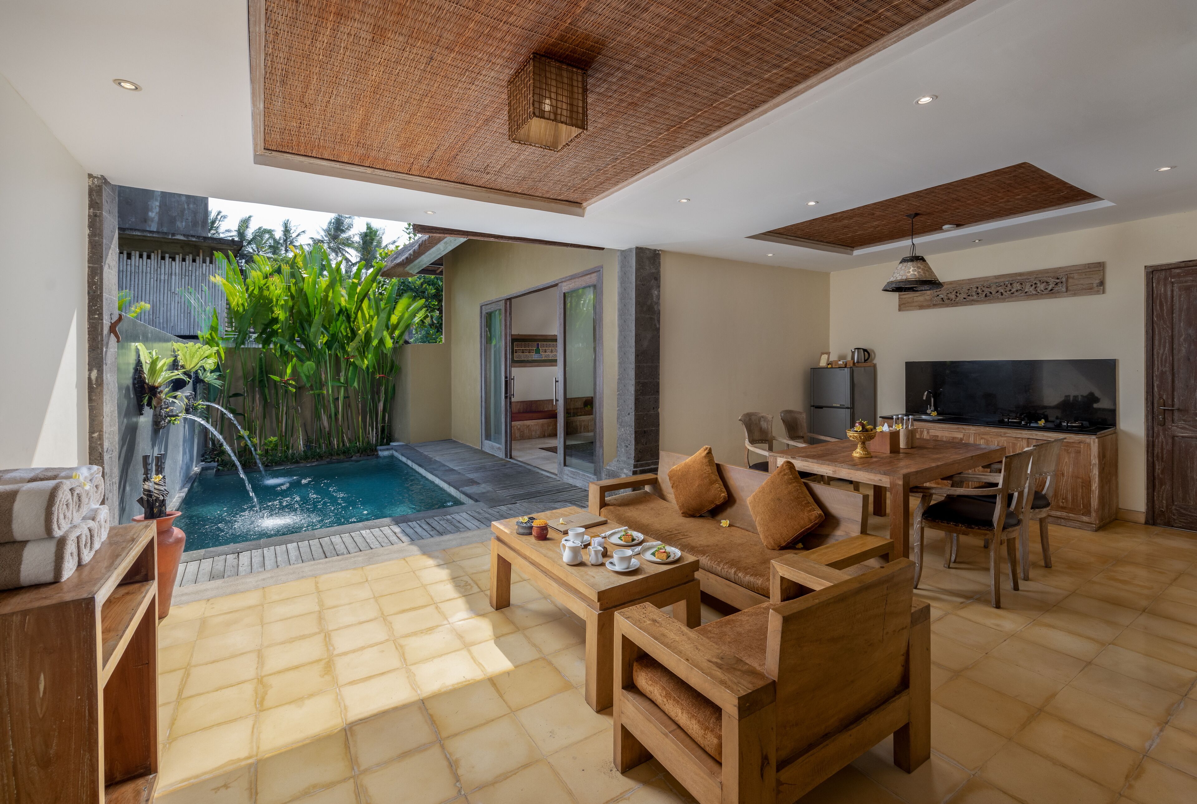 A spacious living area with a pool, wooden furniture, and a kitchen area.