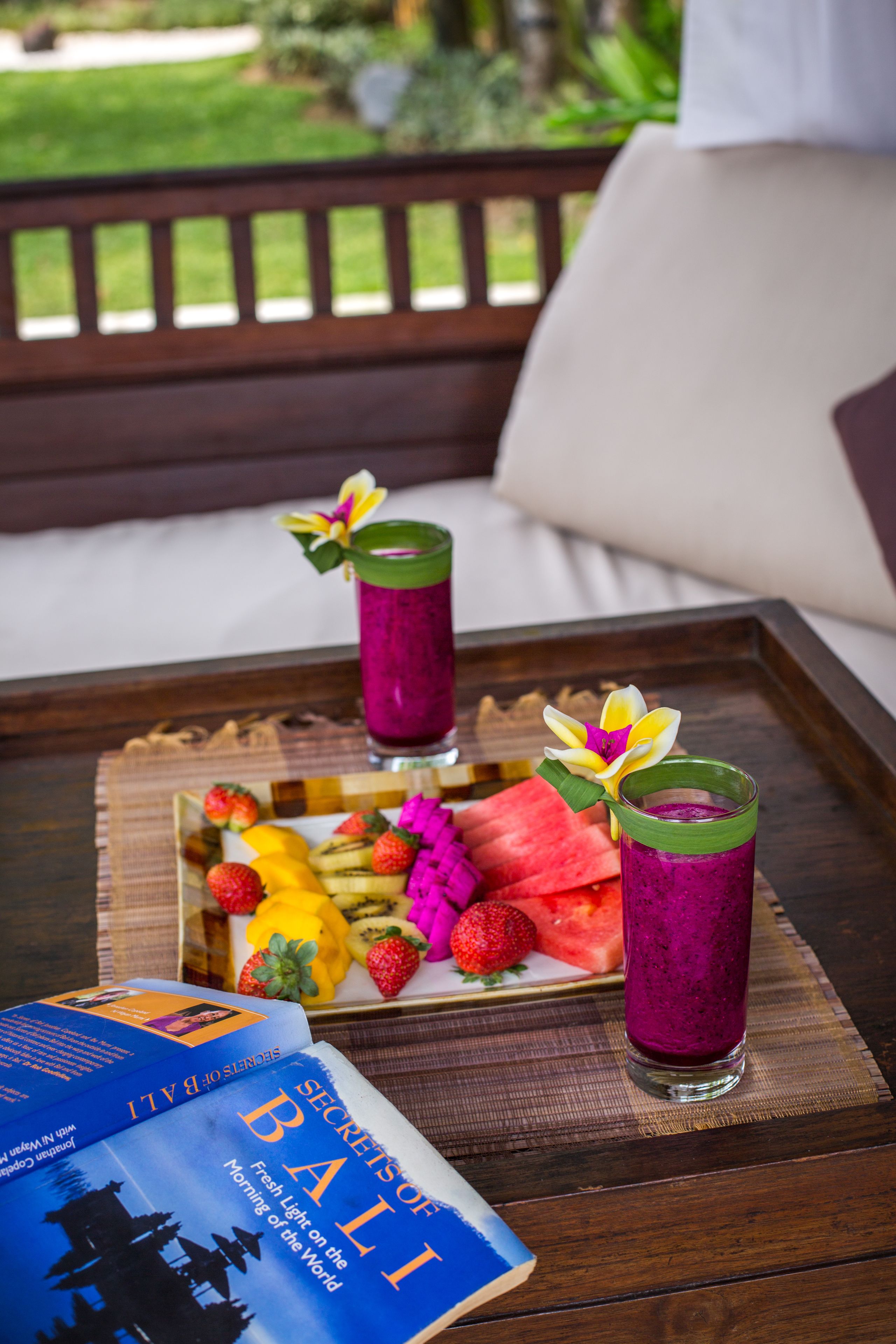 A tray with a book titled "Secrets of Bali" and two drinks on a wooden table.