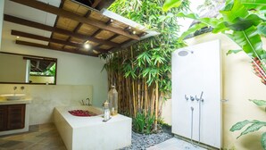 A bathroom with a large bathtub, a shower, and a sink. There is a bamboo wall and a stone pathway leading to the shower. - Villa Seriska Satu Sanur Bali (Denpasar)