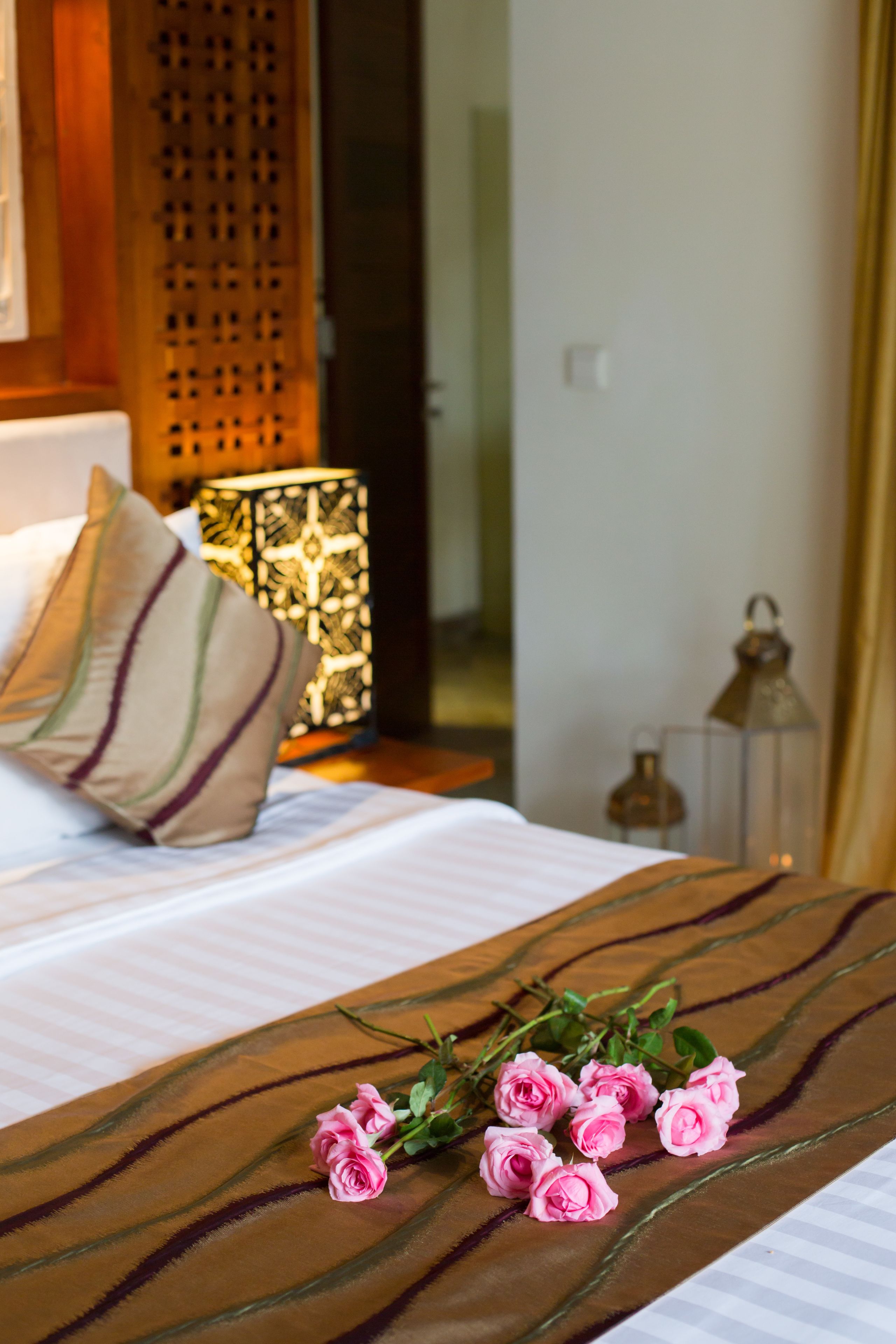 A neatly made bed with a striped pillow, a decorative wall panel, and a bedside table with a lantern.