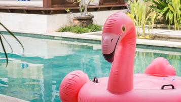 Relax by the serene pool surrounded by lush greenery and a thatched-roof structure.