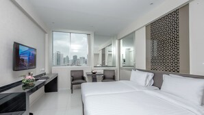 Ein modernes Hotelzimmer mit einem großen Bett, einem Schreibtisch, einem Sessel, einem Fernseher und Blick auf die Stadt.