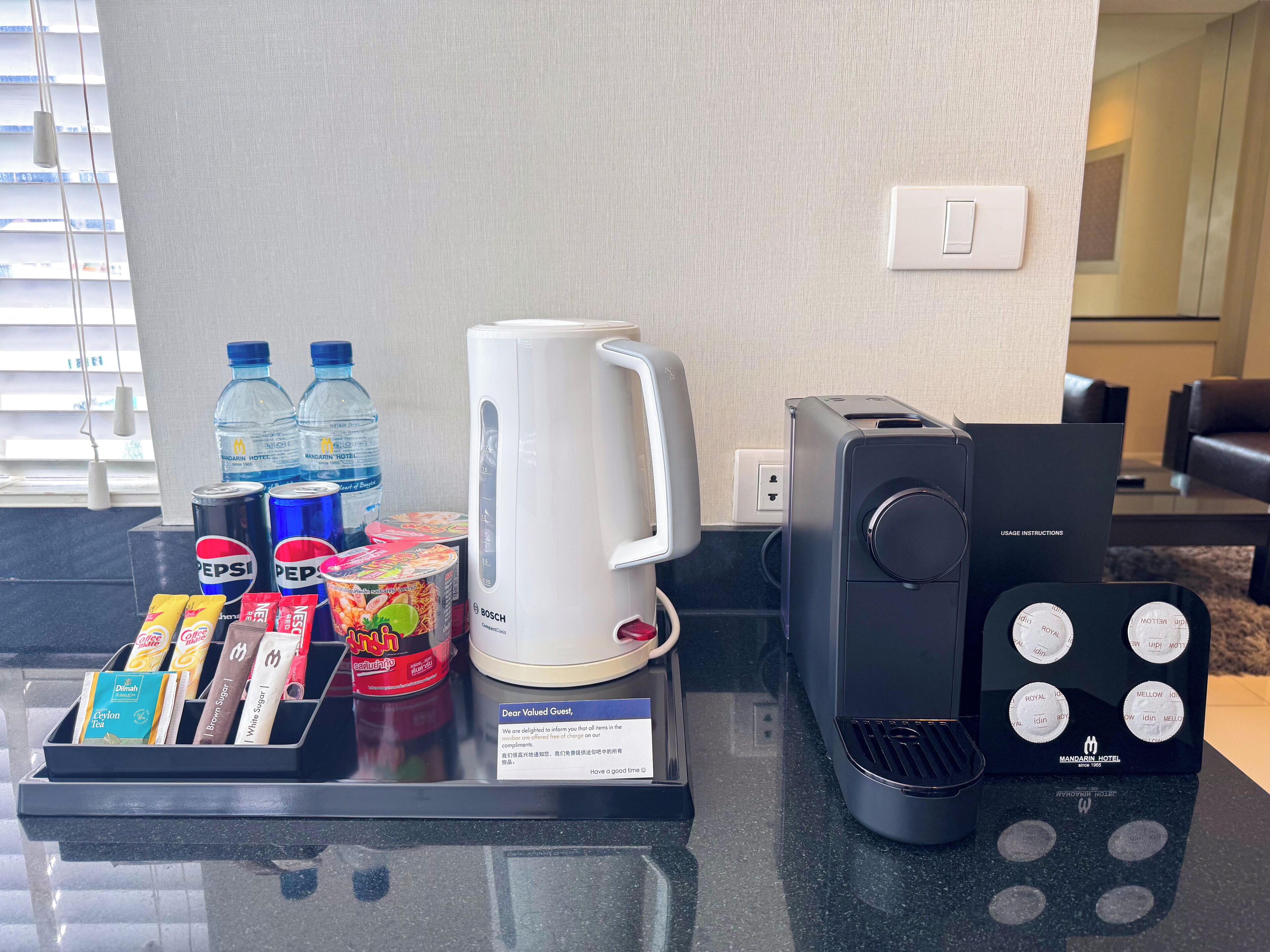 A hotel minibar with a coffee maker, water bottles, snacks, and a tea dispenser.