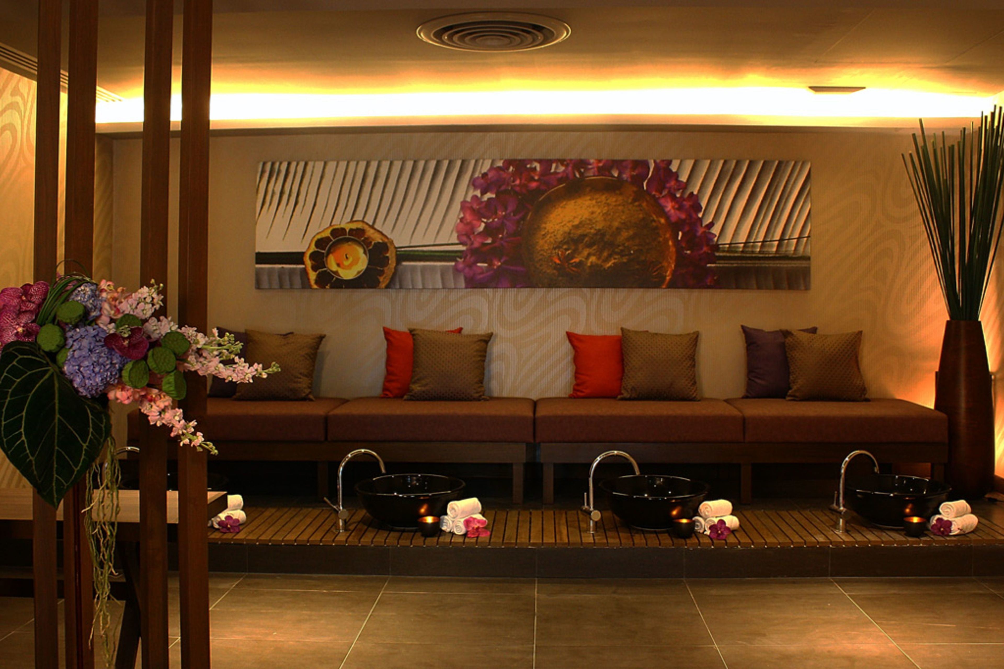 Un área de spa con un sofá, dos lavabos negros y una pared decorativa con una pintura floral.