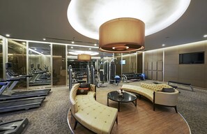 A modern gym with exercise equipment, a lounge area with sofas, and a large circular light fixture.