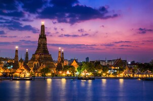 A historic temple complex with multiple structures, including a prominent central tower, surrounded by smaller buildings and a body of water in the foreground.