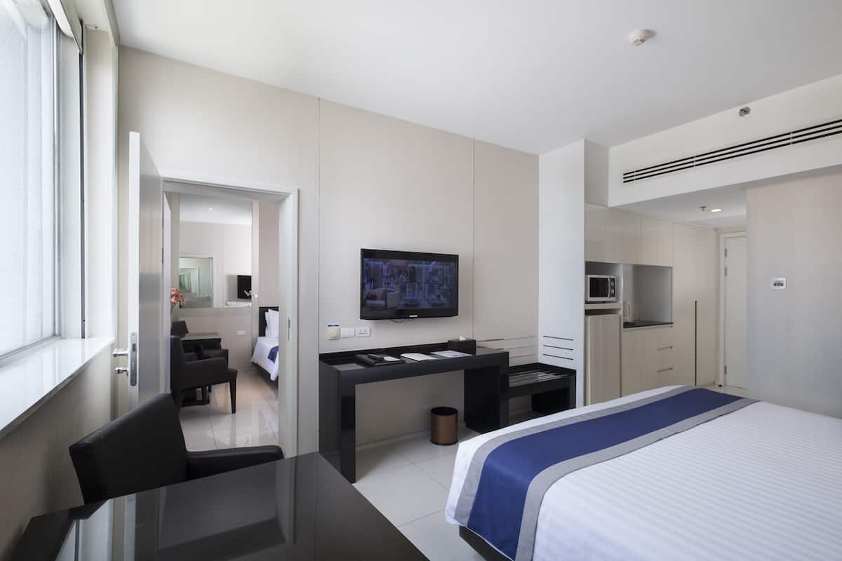 Een moderne hotelkamer met een bed, een bureau met een flatscreen televisie, een magnetron en een kleine kitchenette.