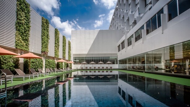 Ein modernes Hotel mit einem zentral gelegenen Pool, Liegestühlen und Sitzbereichen im Freien.