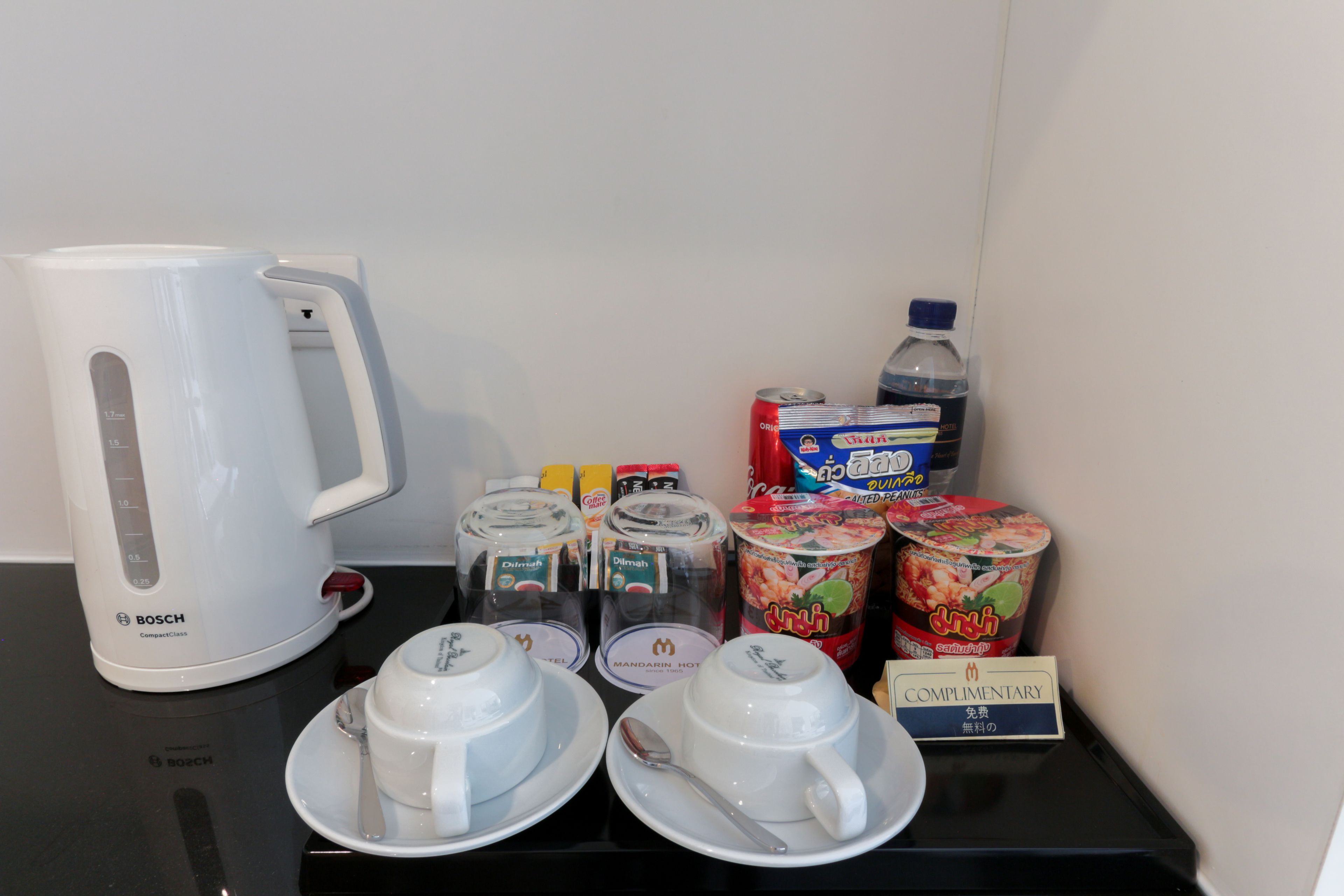 Preparación para el desayuno con una cafetera Bosch, tazas, cucharas, condimentos y un letrero de cortesía.