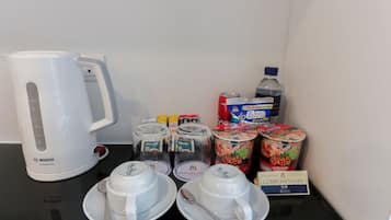 Preparación para el desayuno con una cafetera Bosch, tazas, cucharas, condimentos y un letrero de cortesía.
