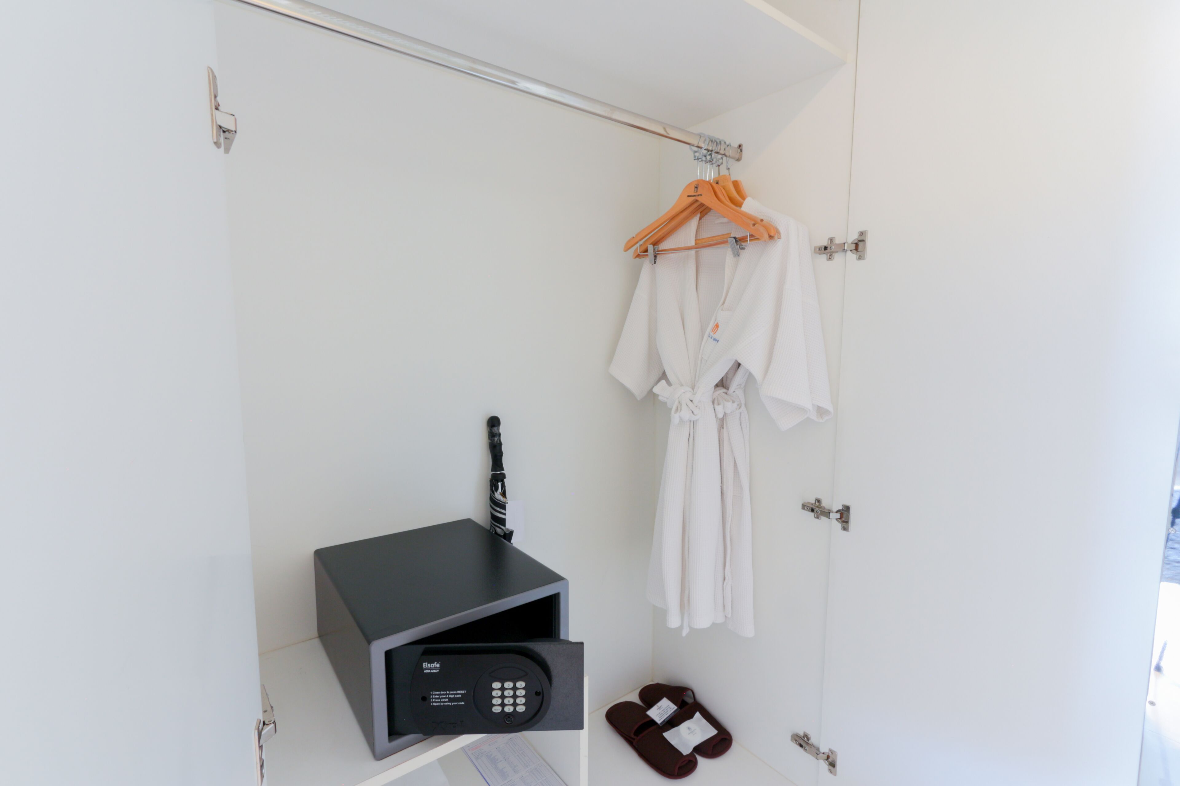 Une salle de bain d’hôtel avec un porte-serviettes, un peignoir, des chaussons et un appareil électronique noir posé sur une étagère.