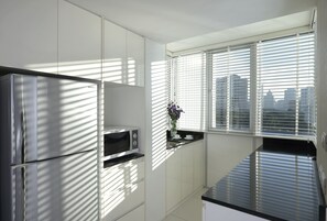 Una cocina moderna con armarios blancos, un refrigerador de acero inoxidable, un microondas y una ventana con persianas.