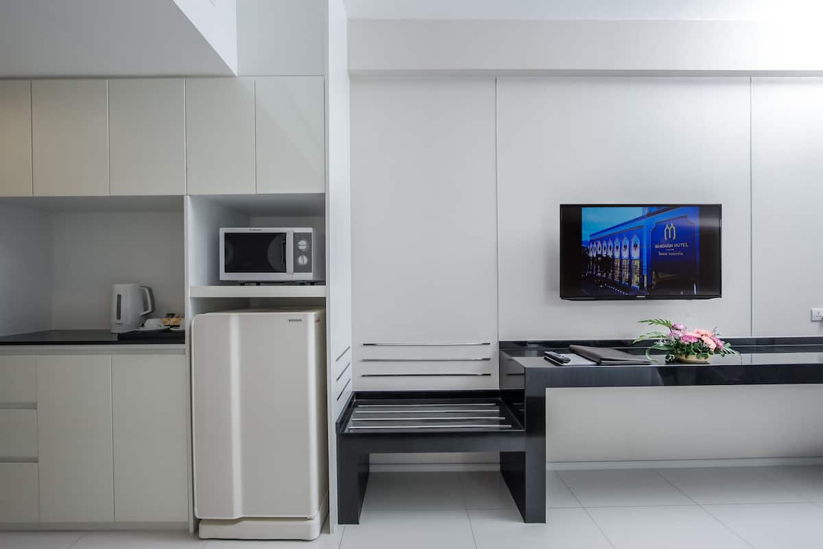 Een moderne keuken met witte kastjes, een ingebouwde magnetron, een koelkast, en een flatscreen televisie aan de muur.
