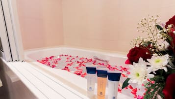 A bathtub with rose petals and three toiletries.
