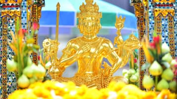 A golden statue of a seated figure with multiple arms, surrounded by colorful, patterned architecture and yellow flowers.