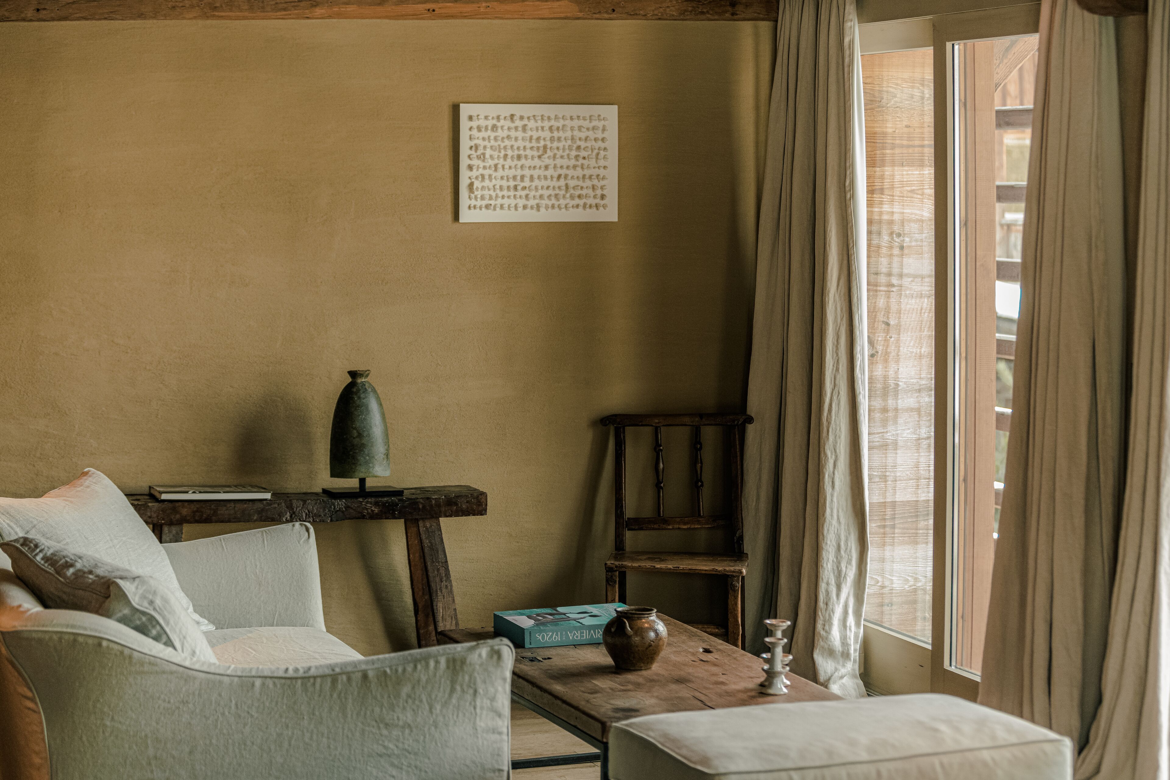 A cozy room with a wooden table, a chair, a small table, and a window with curtains.