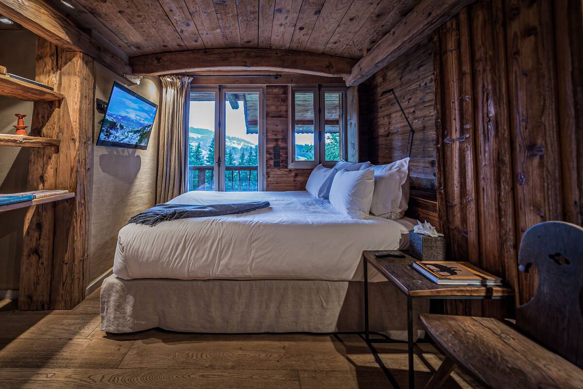 Un dormitorio de cabaña de madera con una cama, un escritorio y un televisor fijado a la pared.