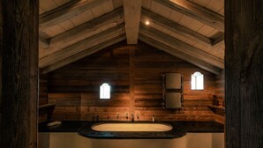 A log cabin bathroom with a large freestanding bathtub, wooden walls, and a sloped ceiling. - Zannier Le Chalet (Megeve)