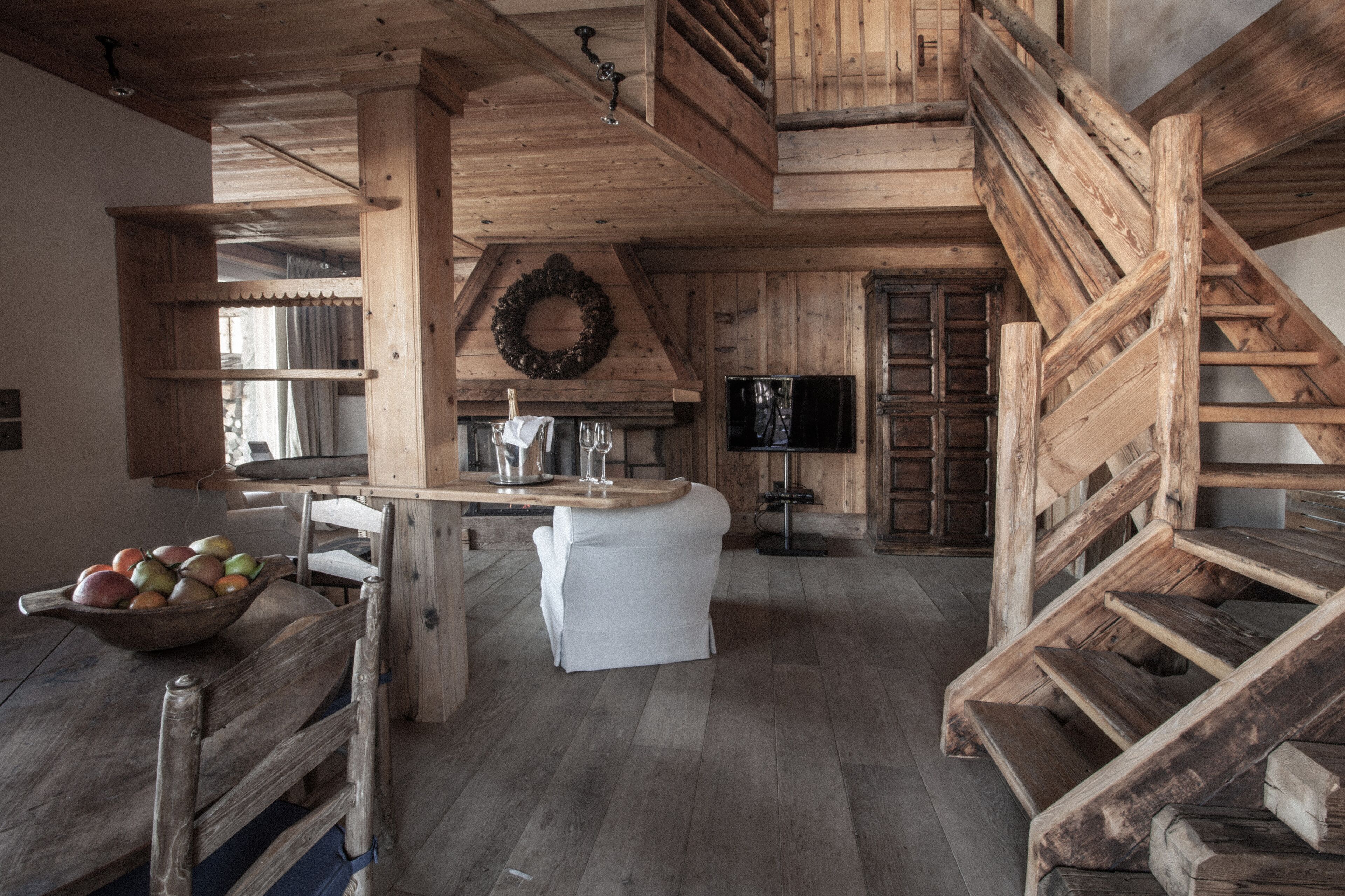 Un intérieur rustique avec un escalier en bois, un coin repas agrémenté d’un panier de fruits et une cuisine équipée d’un téléviseur.