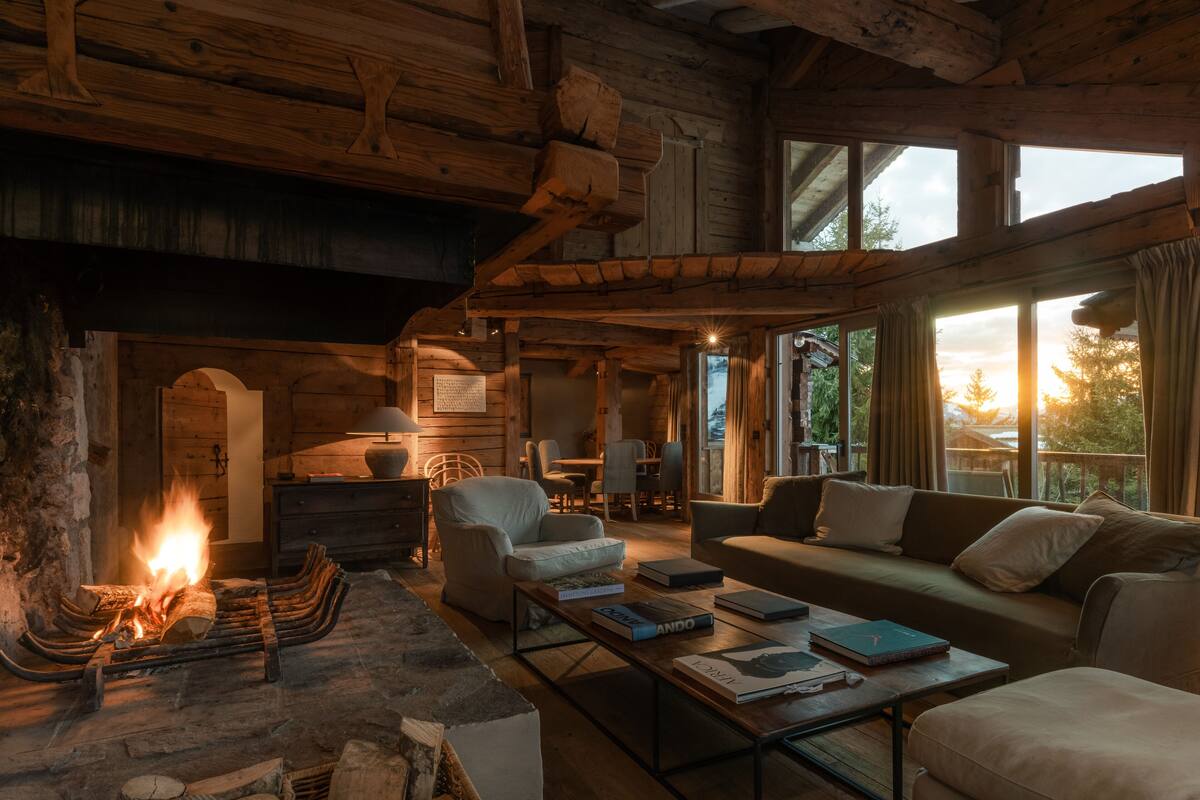 Acogedor interior de cabaña de madera con chimenea, muebles de madera y amplias ventanas que ofrecen vistas al exterior.
