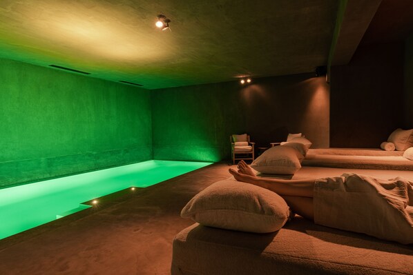 A spa room with a green-lit pool, multiple massage tables, and a chair. - Zannier Le Chalet (Megeve)