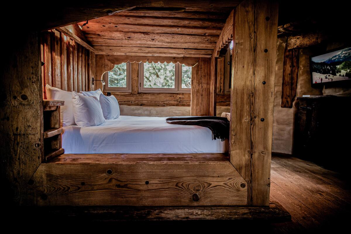 Un dormitorio tipo cabaña de madera con una cama, una ventana y un televisor en la pared.