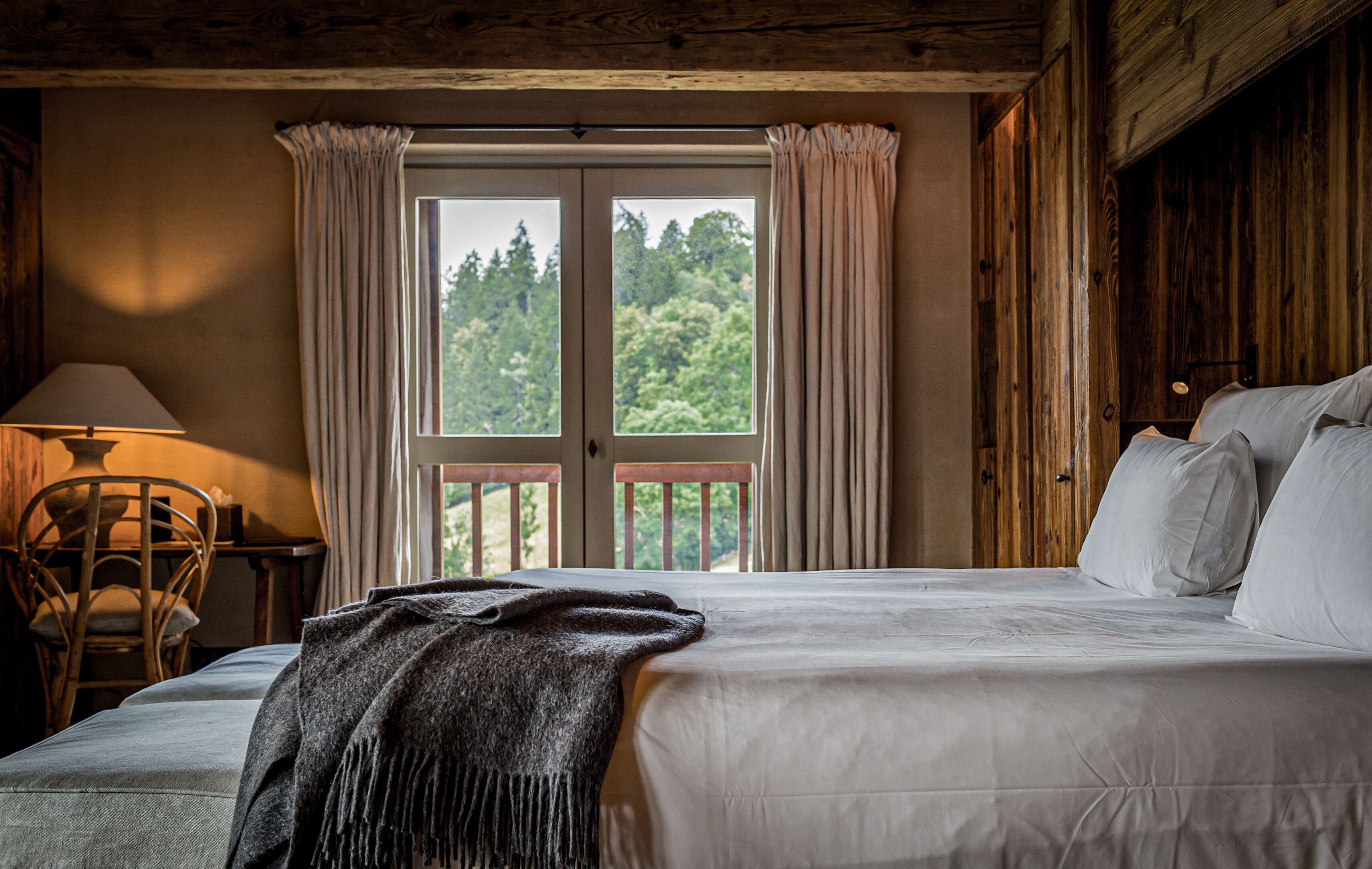 A bedroom with a bed, a chair, a lamp, and a view of greenery through the window.