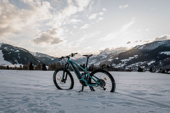 A mountain bike in a snowy field with a backdrop of mountains and a partly cloudy sky.