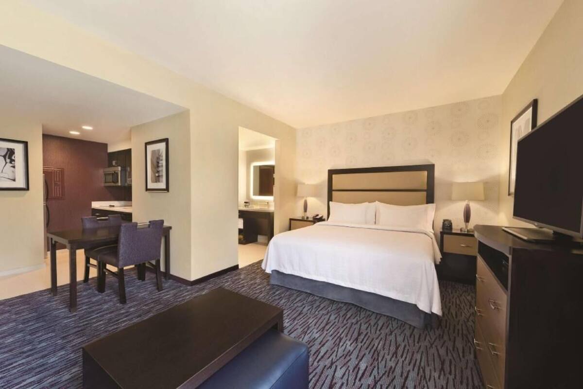 A hotel room with a bed, a desk, a chair, a television, and a dresser.