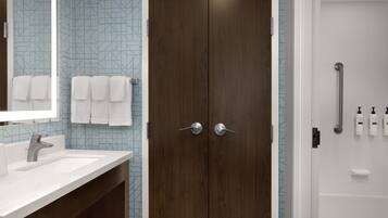Baño con puerta doble, lavabo, espejo y zona de ducha.