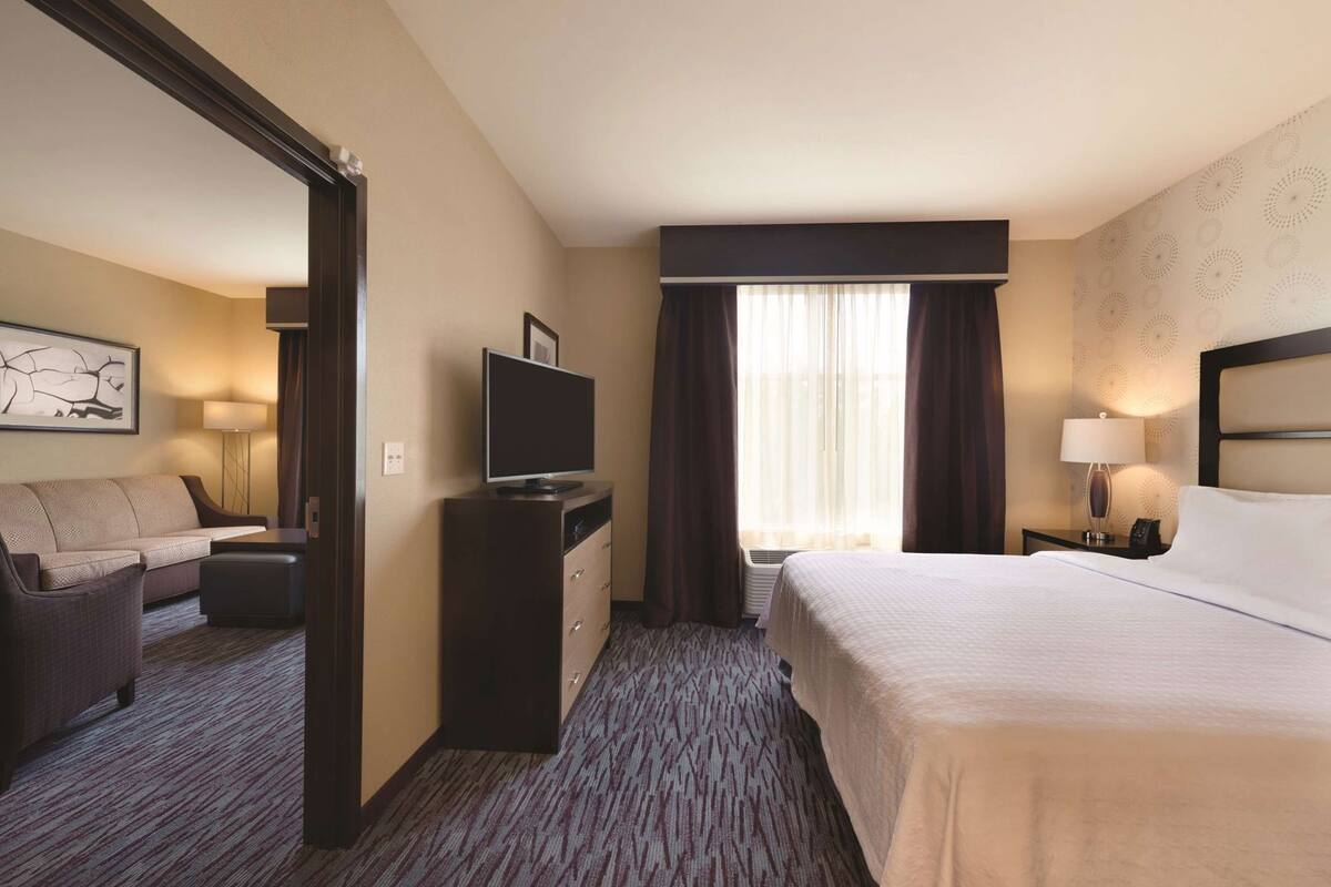 A hotel room with a bed, a desk with a TV, a sofa, and a lamp.