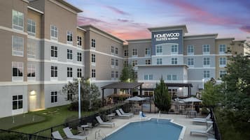 A hotel with a pool, outdoor seating, and a sign for Homewood Suites by Hilton.
