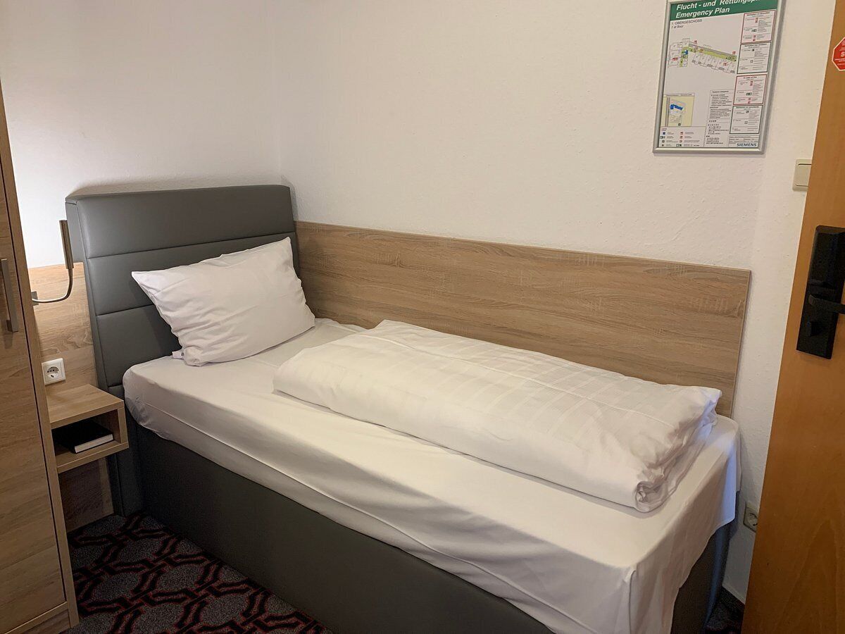 A single bed with a grey headboard and white bedding in a room with a wooden floor and a small bedside table.