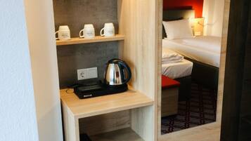 Quarto de hotel compacto com cozinha compacta, uma cama e um pequeno frigorífico.