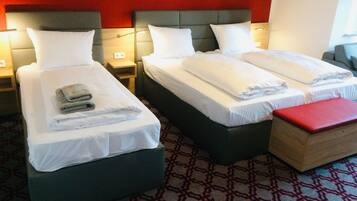 Habitación de hotel con tres camas, cada una con ropa blanca y almohadas, una pared roja y una alfombra estampada.
