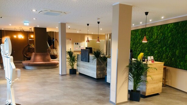 A modern hotel lobby with a reception desk, seating area, and green wall. - Adesso Hotel Göttingen (Goettingen)