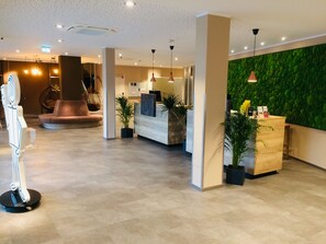 Un moderno vestíbulo de hotel con mostrador de recepción, zona de estar y pared verde.