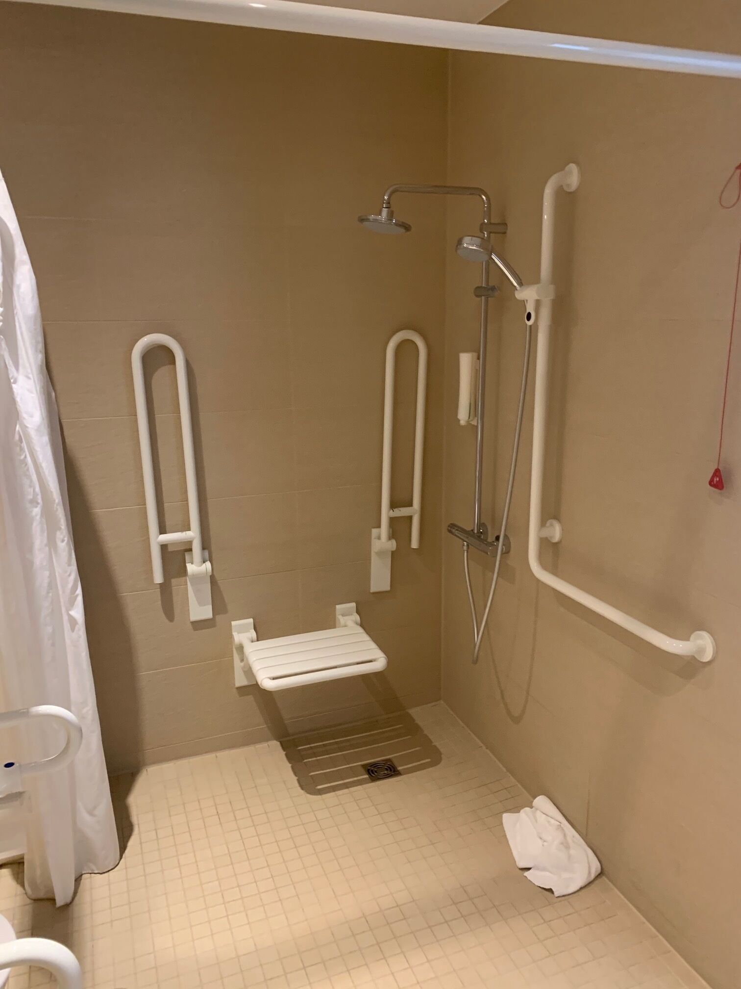 A bathroom with a shower, grab bars, a toilet, and a towel rack.