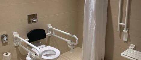 A bathroom with a wheelchair-accessible toilet, a shower curtain, and a handrail.