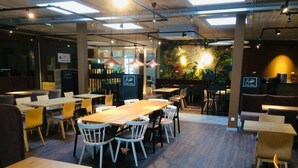 A restaurant with wooden tables and chairs, a mural with tropical plants, and pendant lighting. - Adesso Hotel Göttingen (Goettingen)